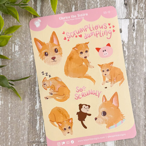 The Clarice the Toxirn ~ Vet Charity Sticker Sheet features adorable dog illustrations, a pink pig face, playful phrases like "scrumptious dumpling" and "so scrungly," all on a light leafy background with a wood surface.