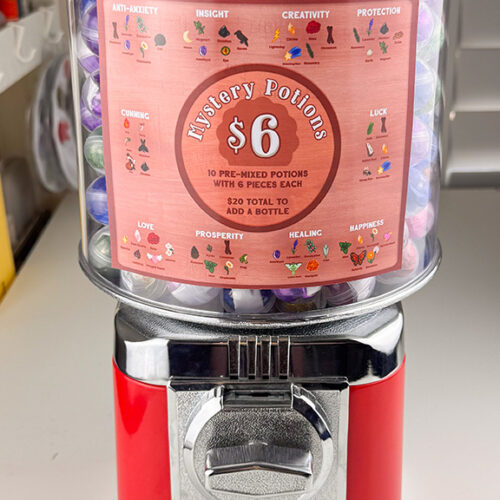 A red and silver gacha machine filled with colorful capsules labeled "Build Your Own Potion ~ Pre-Mixed Potion Pieces" ($6). Themes include anti-anxiety, creativity, luck, love, healing, and more—each marked with a unique icon.