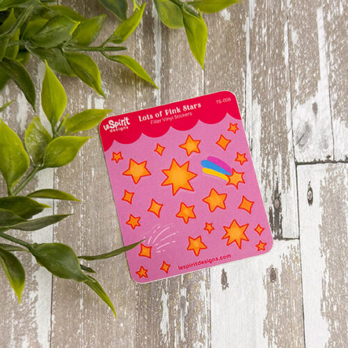A Tiny Pink Stars ~ Tiny Filler Vinyl Sticker Sheet featuring yellow and orange stars, a comet, and a rainbow on pink, displayed on rustic wood beside green foliage. "Lots of Pink Stars" is printed at the top of the sheet.