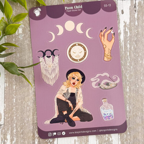 The Moon Child ~ Paper Sticker Sheet features mystical designs on purple: a blonde woman in black, crescent moon, hand with rings, moon phase pattern, crystal ball, macramé wall hanging, smoke, and potion bottle. A green plant is beside it.