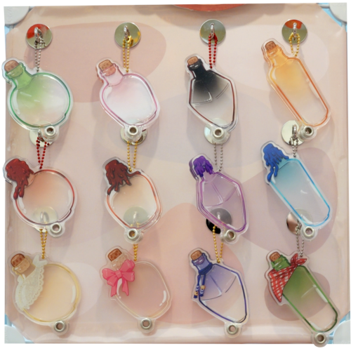 A display of twelve "Build Your Own Potion ~ Openable Shaker Keychains," each shaped like a bottle with different colored liquids and unique decorations such as bows, lace, caps, or hair, arranged in three rows on a soft pink background.