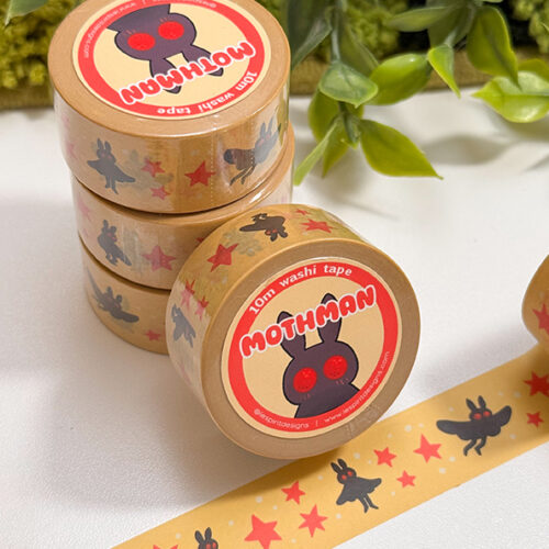 Four rolls of Mothman Washi Tape with a cartoon moth design are stacked beside an unspooled strip, showing red stars and black mothman figures on a beige background with green leaves.