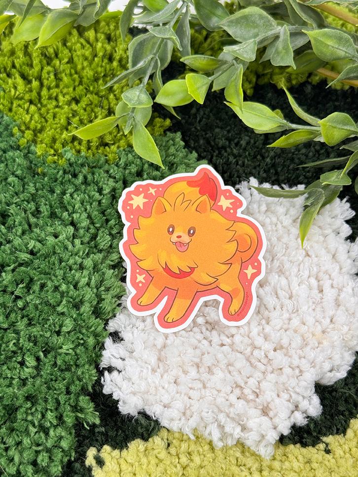 An Uppies Kitty ~ 3" Matte Vinyl Sticker featuring a cute, orange, fluffy cat with a bushy tail rests on a textured, multicolored rug beneath green leafy plant stems.
