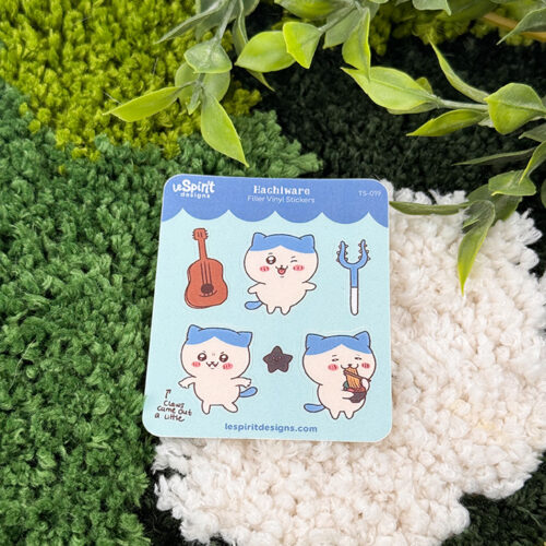 The Tiny Blue Kitty ~ Tiny Filler Vinyl Sticker Sheet features three cute blue and white cat characters, a guitar, and a trident, shown on green and white textured fabric with leafy branches overhead.