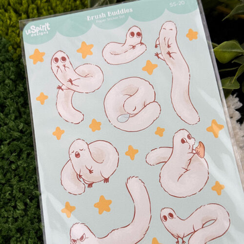 The Puffpuff ~ Paper Sticker Sheet features cute, cartoon snake-like creatures with expressive faces in various poses, surrounded by yellow stars and plants on a light blue background.
