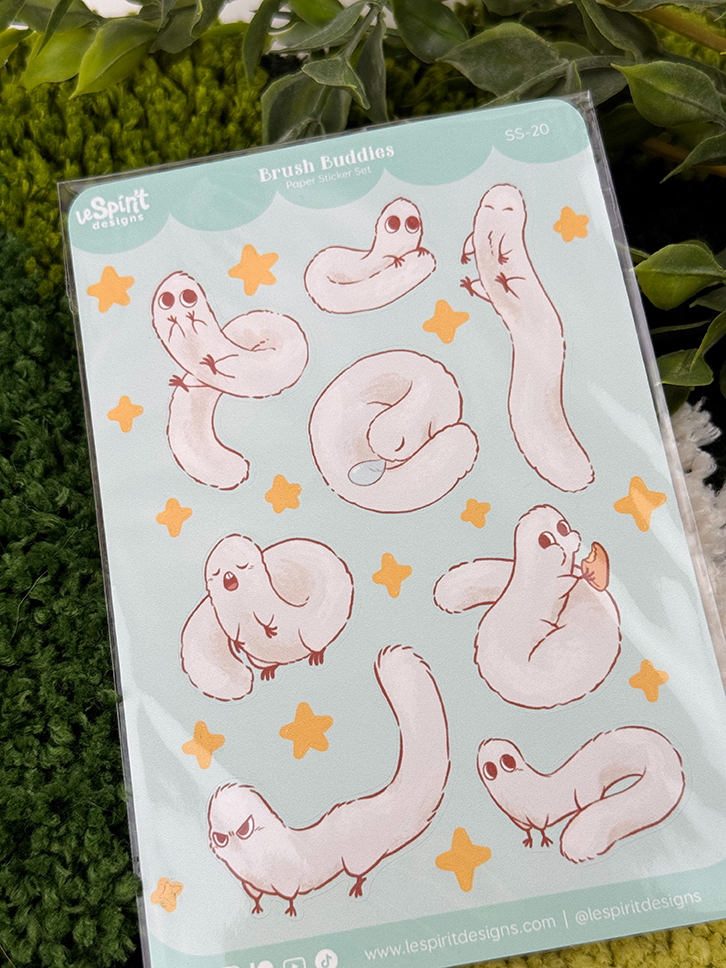 The Puffpuff ~ Paper Sticker Sheet features cute, cartoon snake-like creatures with expressive faces in various poses, surrounded by yellow stars and plants on a light blue background.