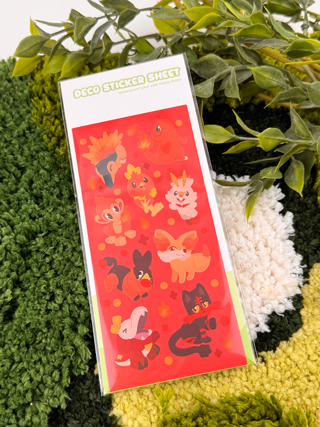 The "Fire Starters ~ Deco Sticker Sheet" features cute, cartoon fire-themed animals on a red background, displayed on a green and cream textured surface with leafy plants nearby.