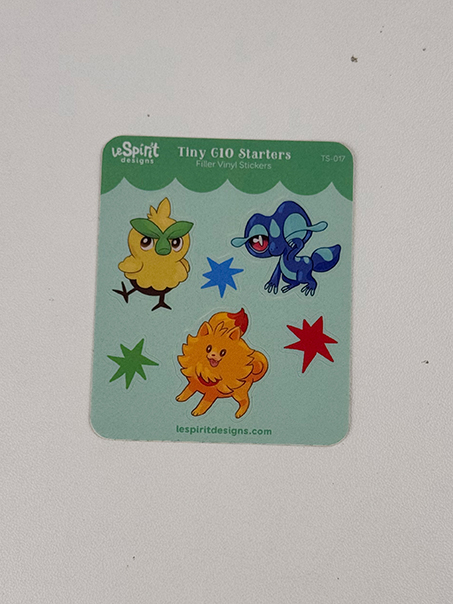 The Tiny Gen10 Starters ~ Tiny Filler Vinyl Sticker Sheet showcases cartoon-style art of a yellow bird, blue frog, orange puppy, and three colorful stars on a light green background.