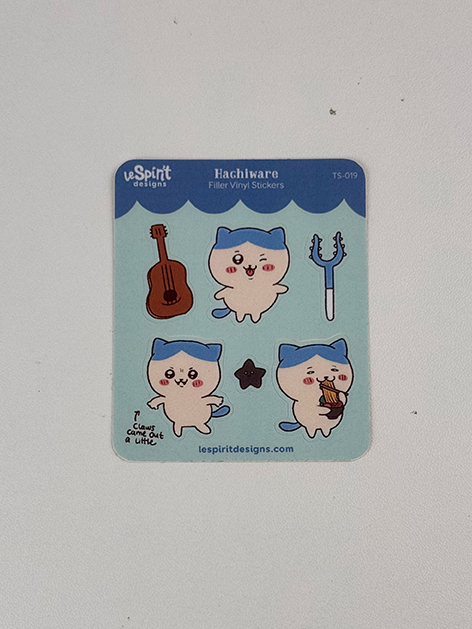 The Tiny Blue Kitty ~ Tiny Filler Vinyl Sticker Sheet features cute cartoon cats in blue hats: one with a guitar, one with a microphone, one eating pudding, and one standing with arms out. Also includes small guitar and music note stickers.