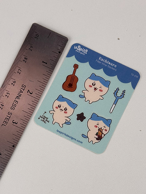 The Tiny Blue Kitty ~ Tiny Filler Vinyl Sticker Sheet features four chubby cat characters in blue hats with various objects (guitar, trident, mic, cupcake), shown beside a stainless steel ruler for size reference.