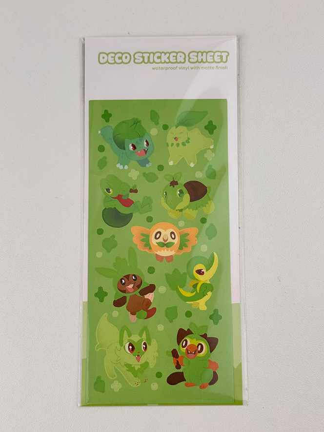 The Grass Starters ~ Deco Sticker Sheet features cute, cartoon-style grass-type Pokémon on a light green background with clover shapes.