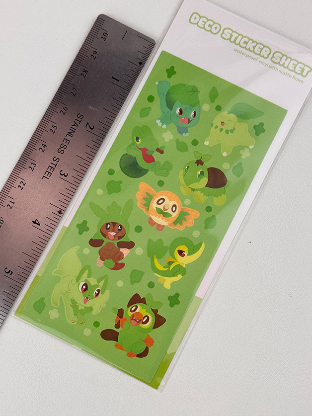 The Grass Starters ~ Deco Sticker Sheet features cute green cartoon animal characters and small green paw prints, shown next to a silver ruler for scale. The sheet is labeled “Deco Sticker Sheet.”.
