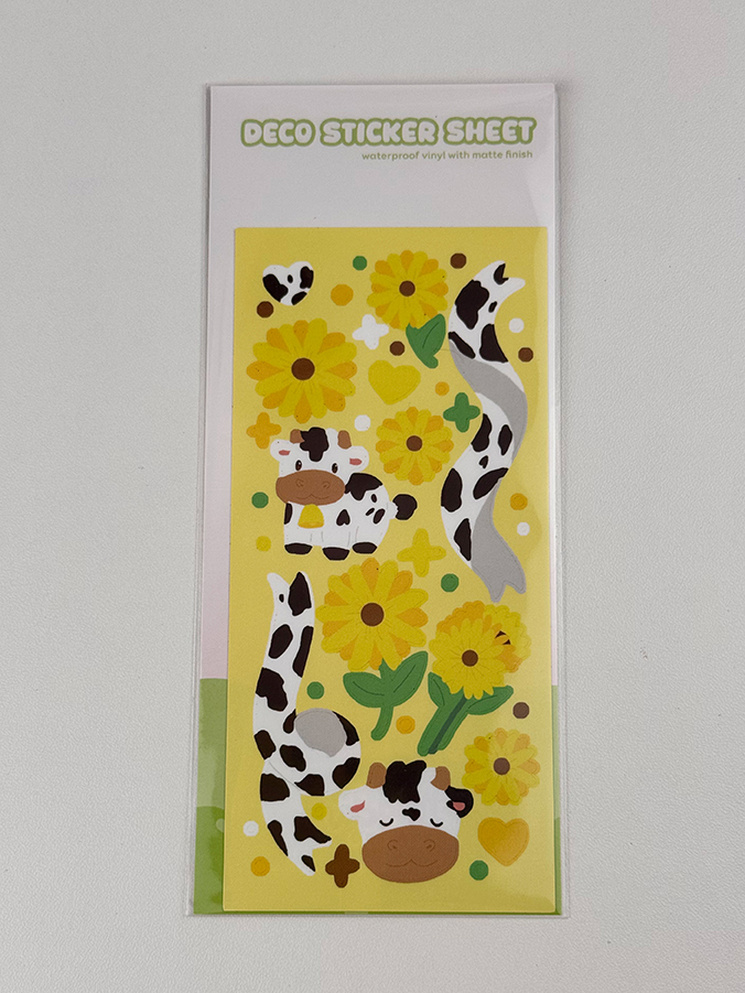 The Sunflower Cows ~ Deco Sticker Sheet features cute cows, yellow sunflowers, green leaves, hearts, and cow prints. The label reads “DECO STICKER SHEET” and notes the stickers are waterproof vinyl with a matte finish.