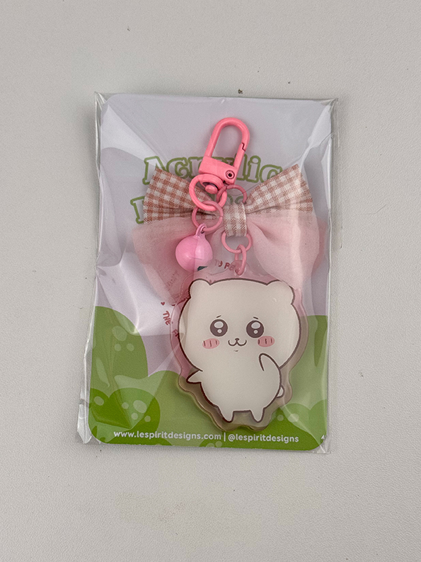 A packaged Pink Hamster ~ Acrylic Keychain featuring a cute white cartoon hamster with pink cheeks, a pink and white plaid bow, and a pink clip with bell, displayed on a green and white card.