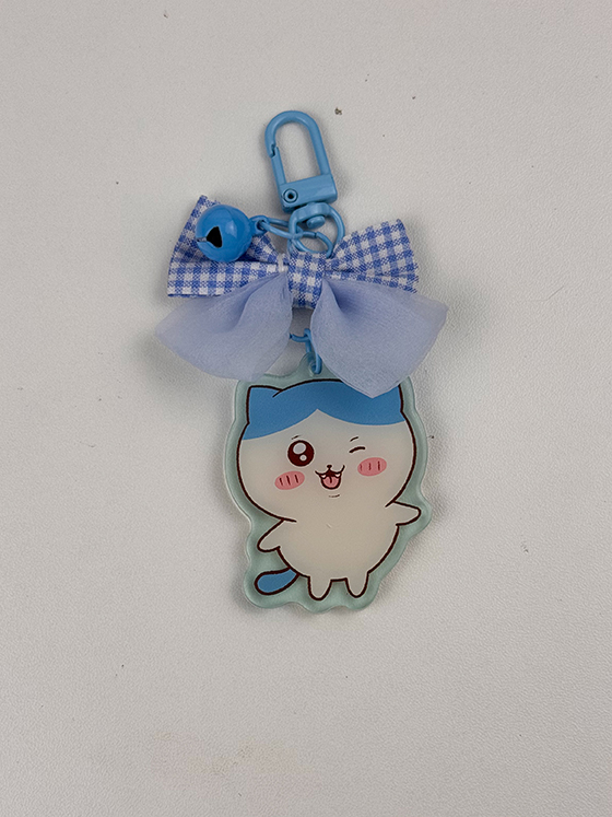 The Blue Kitty ~ Acrylic Keychain features a cartoon cat with blue ears, winking and sticking out its tongue. It includes a blue clip and is adorned with a blue and white checkered ribbon bow.