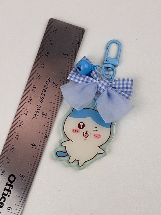 The Blue Kitty ~ Acrylic Keychain features a cute cartoon character with a blue hat, pink cheeks, and a smiling face. Decorated with a blue bow and bell, it measures about 8 cm long when placed next to a stainless steel ruler.