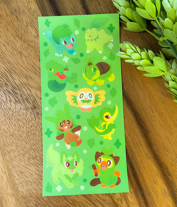 The Grass Starters ~ Deco Sticker Sheet features adorable grass-type Pokémon stickers, shown on a wooden surface with small green plant branches.
