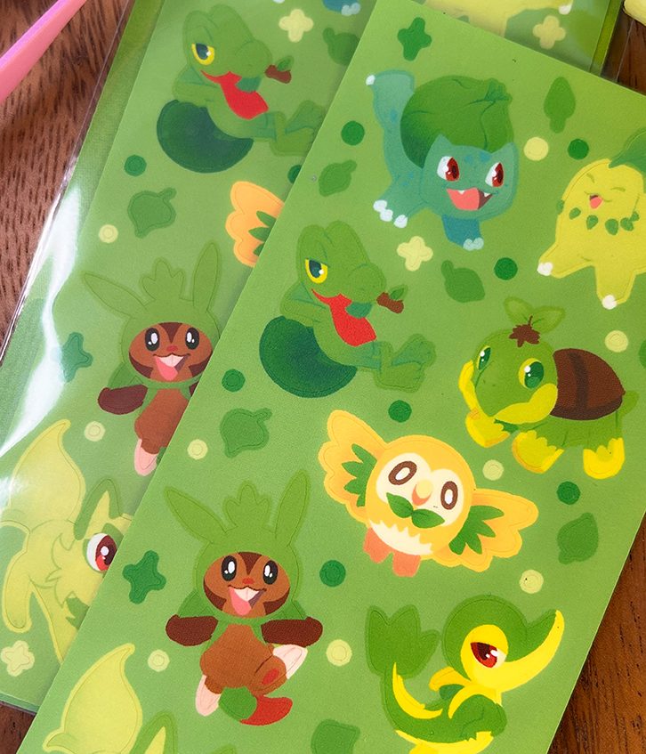 The Grass Starters ~ Deco Sticker Sheet features vibrant stickers of Bulbasaur, Turtwig, Chikorita, Rowlet, Treecko, Snivy, and Chespin on a green plant-themed background.