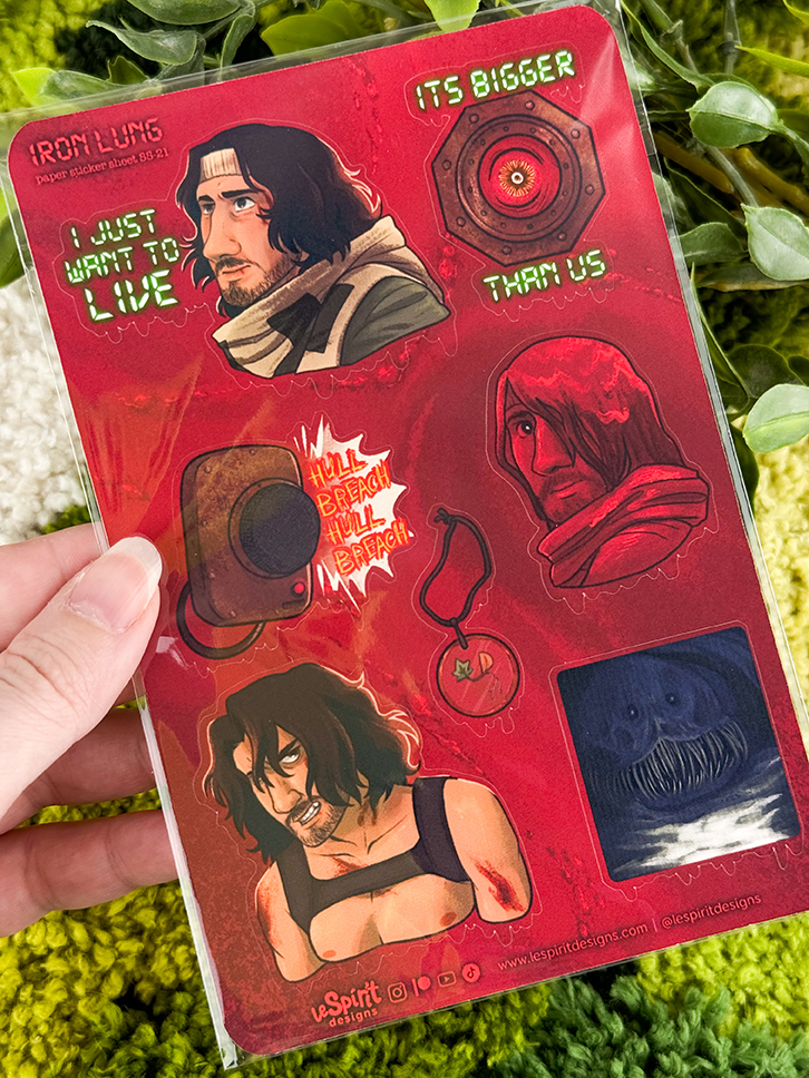 A hand holds a red Iron Lung-themed sticker sheet featuring illustrated characters, a submarine, a keychain, and the phrases I just want to live and Its bigger than us..
