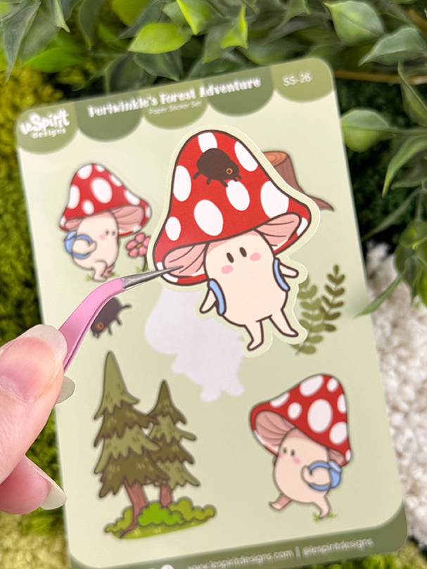 A hand holds tweezers with a sticker of a cute mushroom character, standing on a sticker sheet with more mushroom characters, trees, and leaves on a green background.