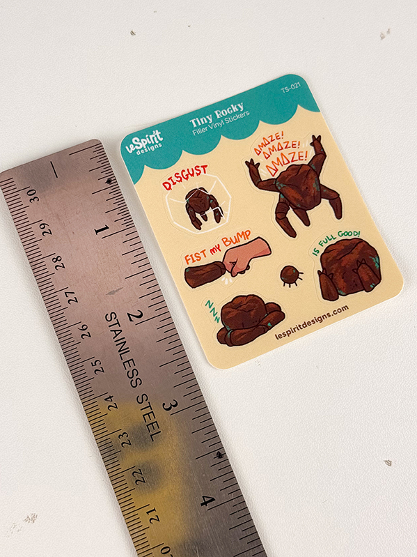 A Tiny Rocky ~ Tiny Filler Vinyl Sticker Sheet featuring small cartoon brown turtle stickers in various poses and expressions, displayed next to a stainless steel ruler for scale.