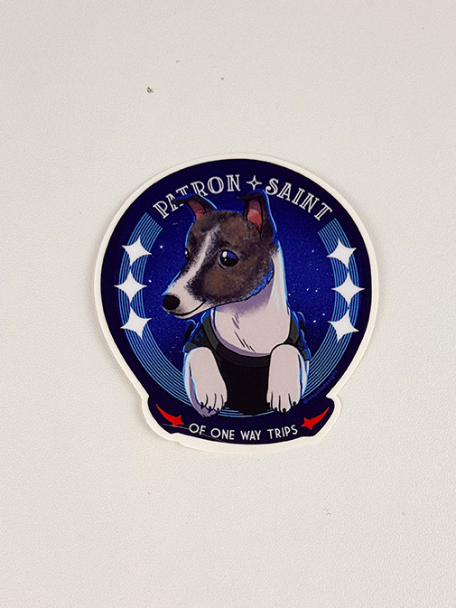 A sticker shows a cartoon dog in a blue suit with stars behind it, surrounded by the text Patron Saint of One Way Trips..