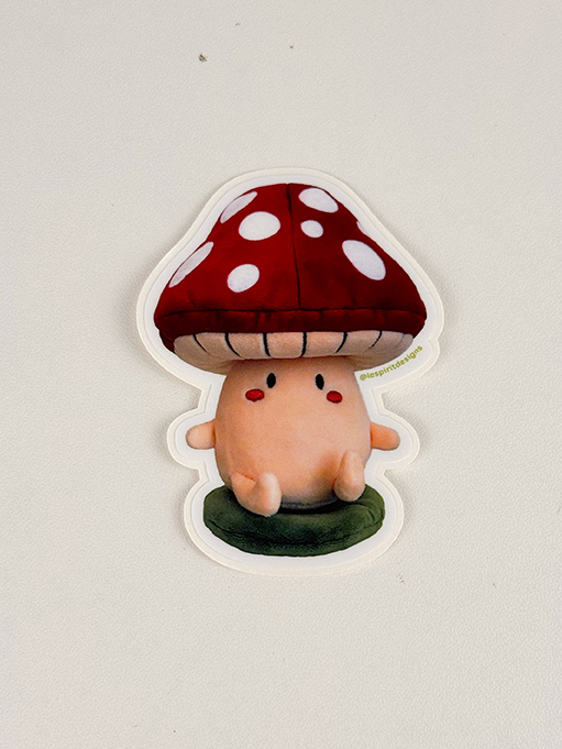 A cute cartoon sticker of a mushroom character with a red cap and white spots, small arms and legs, and two red dots for cheeks, sitting on a green base against a plain background.